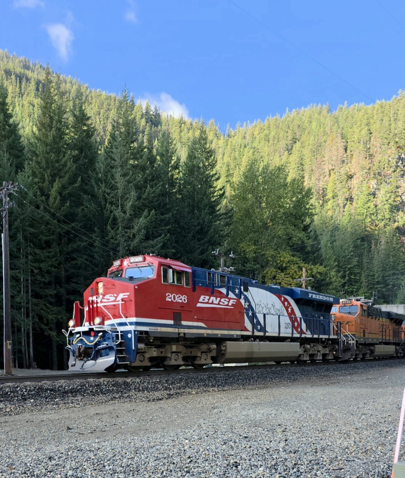 BNSF 2026 in red, white and blue America 250 livery leading a train through a forested mountain pass