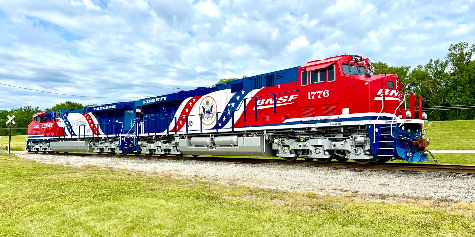 BNSF 1776 leading BNSF 2026, both in America 250 livery, on a grassy line under a cloudy sky